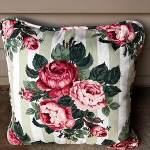 Puede incluir: Una almohada de rayas blancas y verdes con un patr&oacute;n floral de rosas rosas y rojas. La almohada tiene un fondo blanco con rayas verdes y un patr&oacute;n floral de rosas rosas y rojas.