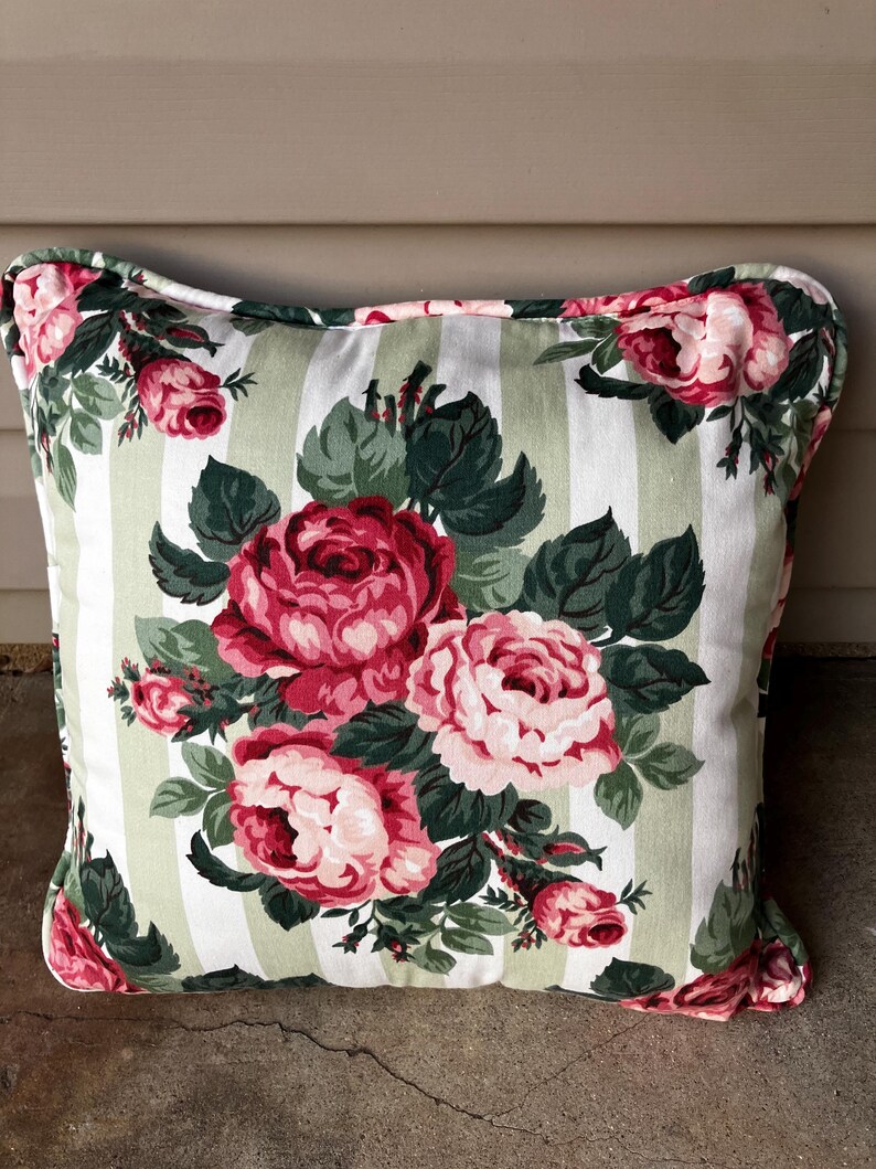 Puede incluir: Una almohada de rayas blancas y verdes con un patr&oacute;n floral de rosas rosas y rojas. La almohada tiene un fondo blanco con rayas verdes y un patr&oacute;n floral de rosas rosas y rojas.