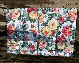 Könnte beinhalten: Weißes Kissenbezug mit floralem Muster. Das Muster zeigt große Rosen in Rot, Gelb und Rosa, mit grünen Blättern und kleinen blauen Blüten. Der Stoff ist wahrscheinlich Baumwolle oder ein ähnliches Material.