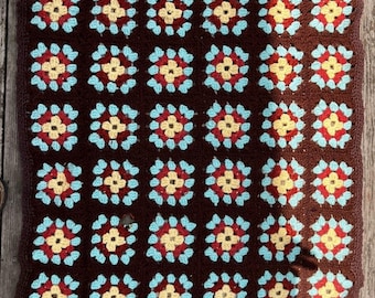 Könnte beinhalten: Eine rechteckige Häkeldecke mit einem sich wiederholenden Granny-Square-Muster. Jedes Quadrat besteht aus einer hellgelben Mitte, einer dunkelroten Zwischenschicht und einem hellblauen Rand, verbunden durch ein dunkelbraunes Garn.