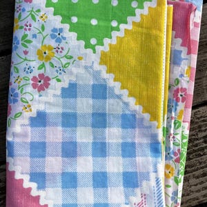 May include: A stack of colorful fabric pieces with a patchwork design. The fabrics feature patterns like gingham, floral prints, and polka dots in shades of green, yellow, pink, and blue. The edges have a decorative, scalloped trim.