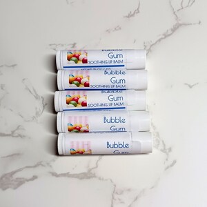 May include: Five white lip balm tubes with labels featuring colorful gumballs and the text "Bubble Gum Soothing Lip Balm." The tubes are arranged vertically on a white marble surface.