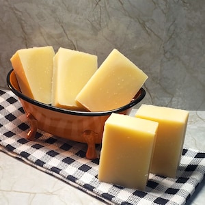 May include: Five bars of plain white soap in a brown ceramic bowl with a white and black checkered tablecloth underneath.