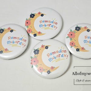 May include: Four white round buttons with a yellow crescent moon and colorful flowers. The text "Ramadan Mubarak!" is written in colorful letters on each button.