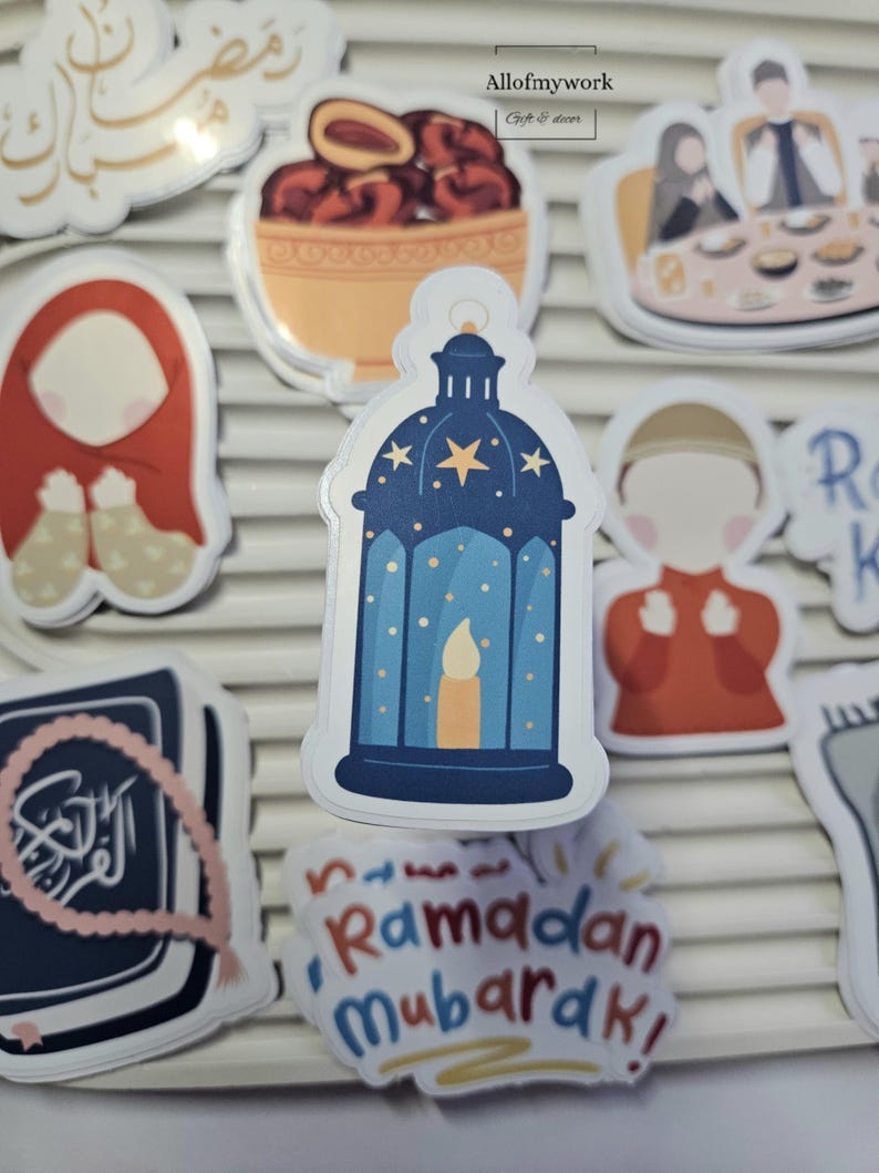 May include: A set of Ramadan themed stickers featuring a blue lantern with stars and a candle, a red and white prayer rug, a bowl of dates, a book with Arabic script, and a sticker that says "Ramadan Mubarak!"