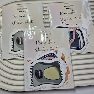 May include: Three packs of Ramadan sticker packs. Each pack has a different design featuring a mosque, a prayer rug, and a book with a tassel. The text on the packs reads "Allofmywork Ramadan Sticker Pack".