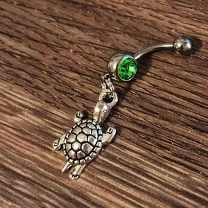 May include: Silver belly button ring with a green gem and a dangling turtle charm.