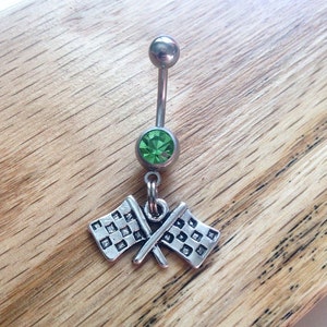 May include: A silver belly button ring with a green gem and a charm of two crossed checkered flags.
