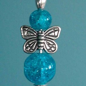Puede incluir: Un dije de mariposa plateado con cuentas de vidrio azul turquesa en un alfiler plateado.