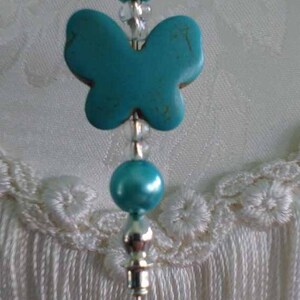May include: A turquoise butterfly charm with silver beads and a silver pin. The charm is hanging from a silver pin with a silver ball at the top.