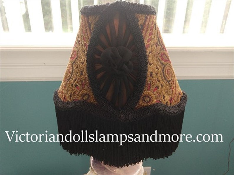 May include: A lampshade with a black fringe and a gold and red patterned fabric. The fabric has a paisley design with a black velvet center.