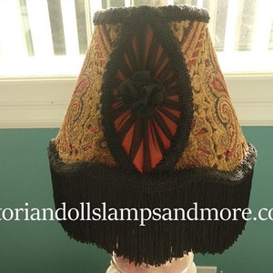 May include: A black and gold lampshade with a fringe trim. The lampshade has a red and black floral design with a black and gold trim.