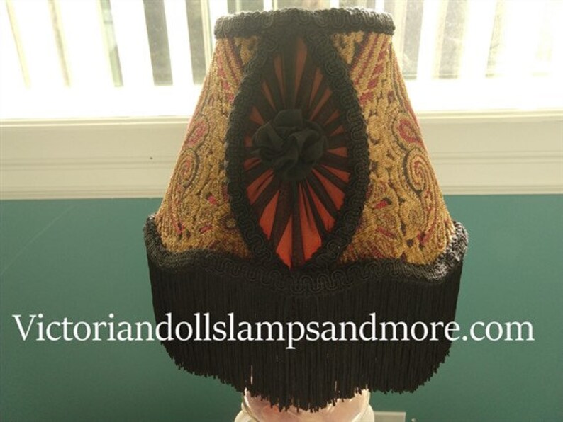 May include: A black and gold lampshade with a fringe trim. The lampshade has a red and black floral design with a black and gold trim.