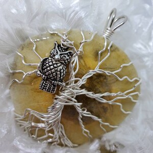 Peut inclure: Un pendentif en fil d'argent enroulé autour d'un arbre de vie avec un charme de hibou en argent. Le pendentif est posé sur une pierre d'agate jaune avec un motif naturel.