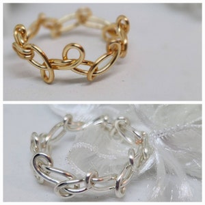 May include: Two rings are displayed, one gold and one silver. The gold ring is a chain-link design with a decorative loop. The silver ring has a similar chain-link design. Both rings are on a white background.