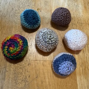 Puede incluir: Seis bolas de ganchillo hechas a mano en varios colores están dispuestas sobre una superficie de madera. Las bolas incluyen tonos de azul, marrón, arcoíris, beige, blanco y azul grisáceo. Las bolas son redondas y tienen un aspecto texturizado.