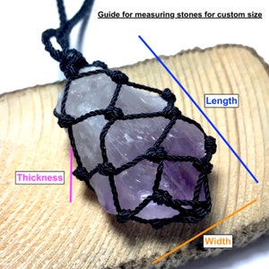 Op de afbeelding: Een ruwe amethist kristallen hanger in een zwart macrame net. De afbeelding bevat een gids voor het meten van stenen voor een aangepaste maat, met labels voor lengte, dikte en breedte. De amethist is lichtpaars van kleur.