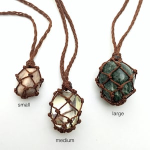 以下が含まれることがあります： さまざまなサイズの3つの宝石ネックレス。 各石は茶色の織りネットで囲まれ、お揃いの茶色のコードから吊り下げられています。 小さな石は薄いピンク色、中くらいの石は黄色、大きな石は緑色です。 サイズを示すテキストラベルがあります。