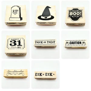 May include: A collection of eight wooden rubber stamps featuring Halloween-themed designs including a tombstone with RIP, a witch hat, a BOO sign, an Admit 1 October 31 ticket, Trick or Treat text, a Caution sign with skulls, Spooktacular, and EEK EEK.