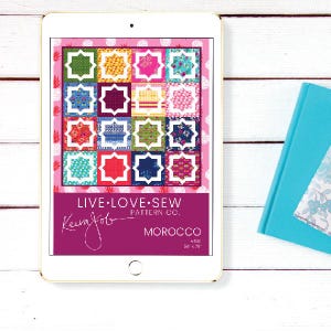 May include: A digital tablet displays a colorful quilt pattern titled "Morocco" by Live Love Sew. The quilt design features a grid of squares with star-shaped and geometric patterns in various colors. A teal book is partially visible.