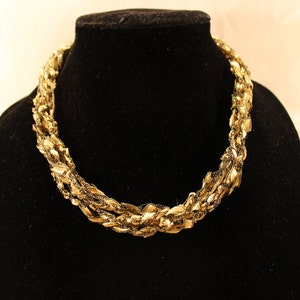 May include: A gold-toned necklace made of interwoven chains, displayed on a black velvet mannequin bust.