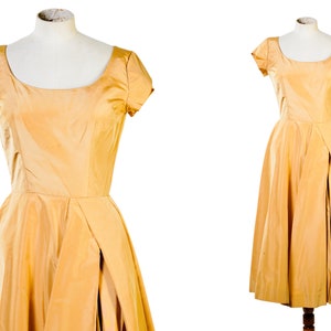 May include: A gold satin dress with a scoop neckline and short sleeves. The dress has a fitted bodice and a full skirt with a side slit.