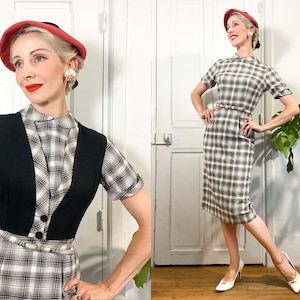 Könnte beinhalten: Ein Outfit im Vintage-Stil mit einem karierten Kleid und einer schwarzen Weste. Das Kleid hat kurze Ärmel und eine figurbetonte Silhouette. Das Outfit wird mit einem roten Hut und weißen Absätzen ergänzt. Der Look ist klassisch und elegant.