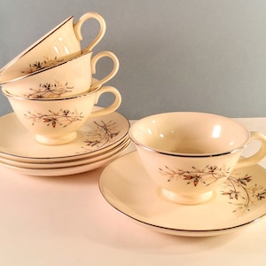 May include: Set of four vintage teacups and saucers with a delicate floral pattern in shades of brown and gold. The cups and saucers are made of white porcelain and have a gold rim.