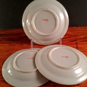 May include: Three white ceramic saucers with red "JAPAN" markings on the bottom.