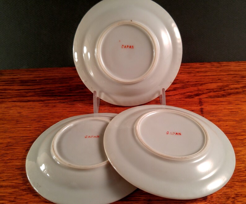 May include: Three white ceramic saucers with red "JAPAN" markings on the bottom.