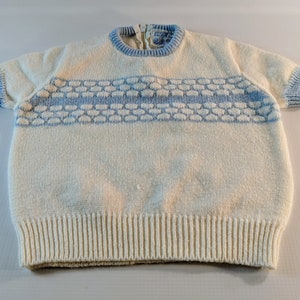 May include: Cream-colored knit short-sleeve sweater with light blue trim on the collar and sleeves. A horizontal band of light blue honeycomb-like pattern is across the chest. The sweater has a ribbed hem and a zipper at the back of the neck.