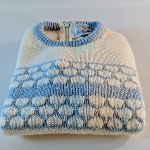 May include: Cream-colored knit sweater with a light blue honeycomb pattern across the chest. The sweater has a light blue ribbed collar and a zipper closure at the back. The label reads "Baby".
