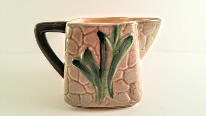 May include: A brown and beige ceramic pitcher with a green and black leaf design. The pitcher has a handle and a textured surface.