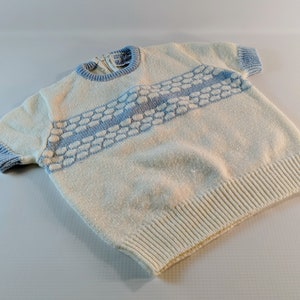 May include: Cream-colored knit sweater with short sleeves and a light blue trim. The sweater features a horizontal band of light blue textured design across the chest. The neckline and sleeve cuffs are also light blue.
