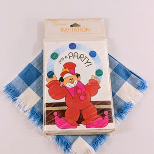 May include: A package of vintage party invitations featuring a cartoon clown juggling colorful balls. The clown is dressed in a red outfit with pink accents. The invitations are packaged in clear plastic and rest on a blue and white checkered cloth.