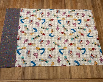 May include: A white fabric pillowcase with a repeating pattern of Alice in Wonderland characters, including Alice, the Cheshire Cat, and the Mad Hatter. The pillowcase has a gray and white polka dot border.