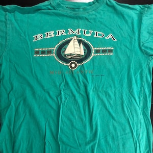 May include: A teal green t-shirt with a white sailboat graphic and the text "BERMUDA MID ATLANTIC" in gold lettering.