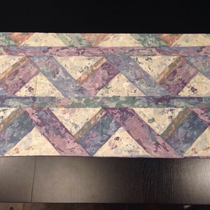 May include: A fabric sample with a geometric pattern of purple, blue, green, and brown triangles on a white background.