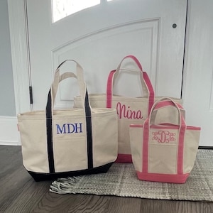 K&ouml;nnte beinhalten: Drei Stofftaschen mit schwarzen, rosa und dunkelblauen Griffen. Die Taschen sind mit den Namen "MDH", "Nina" und einem Monogramm personalisiert.