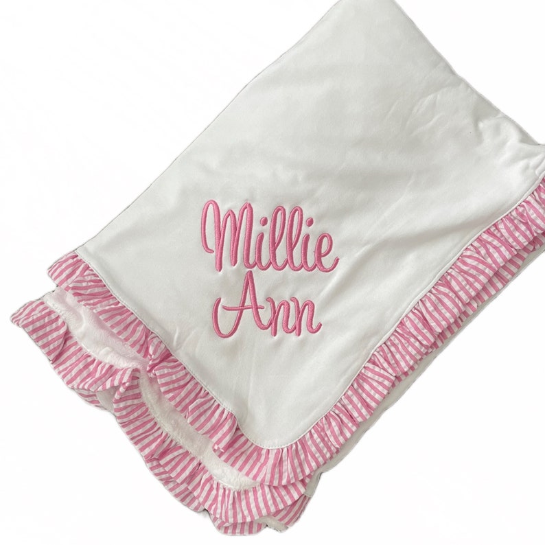 A white baby blanket with pink and white ruffled edges