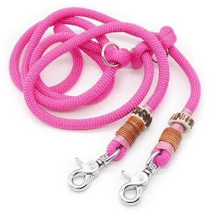 Könnte beinhalten: Rosa doppeltes Hundeleine mit zwei silbernen Clips und braunen Lederakzenten. Die Leine hat einen kleinen Metallring an einem Ende.