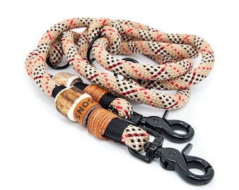 May include: A beige, black, and red patterned rope dog leash with two black metal clips and a brown leather tag that says "SNOS".