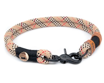 Op de afbeelding: Een beige, zwart en rood geruit touwhalster voor honden met een zwarte metalen gesp en een bruin leren label met de tekst "For the love of dogs".