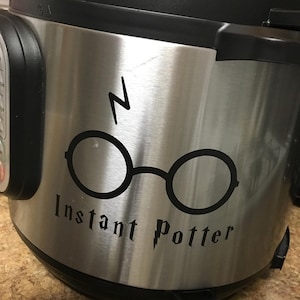May include: A stainless steel Instant Pot with a black decal of Harry Potter's glasses and lightning bolt. The text "Instant Potter" is written in a stylized font below the glasses.