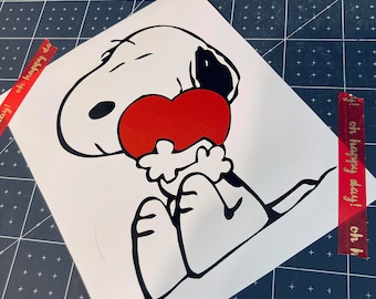 Peut inclure: Illustration de bande dessinée en noir et blanc de Snoopy tenant un cœur rouge. L'image est sur un fond blanc.