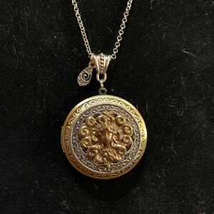 Maiden photo locket hanging from a 24 inch chain, brass and ox finish. She has long flowing hair.