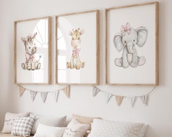 May include: Three framed watercolor prints featuring a zebra, giraffe, and elephant, each adorned with a pink bow. The prints are in light wood frames, hanging above a bench with pillows and a decorative banner.