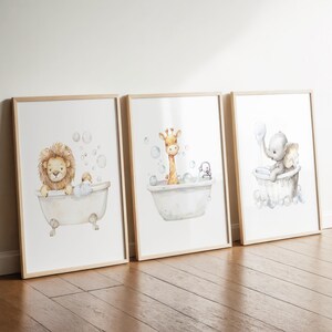 May include: Three framed watercolor prints featuring adorable animals in bathtubs. A lion, giraffe, and elephant are depicted, each enjoying a bubble bath. The prints have a light wood frame and are set against a white background.