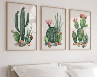以下が含まれることがあります： サボテンと多肉植物を描いた水彩画が3枚、額装されています。最初の絵は、ピンクの花が咲いた背の高いサボテンを描いています。2枚目は、ピンクの花が咲いたサボテンと緑色の多肉植物を描いています。3枚目は、ウチワサボテンと緑色の多肉植物を描いています。