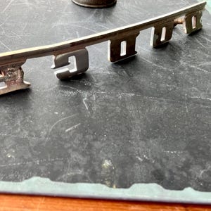 May include: A silver metal key-shaped emblem with the word "FORD" embossed on it.